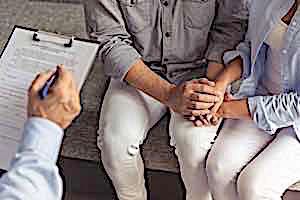 man and woman holding hands while psychologist takes notes