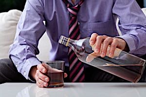 man filling a glass from a bottle of alcohol
