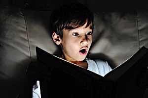 shocked boy reading book with flashlight
