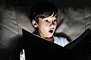 shocked boy reading book with flashlight