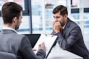 Nervous man in formal wear looking at boss writing on clipboard during job review