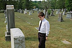 sad boy in cemetary looking at grave stone