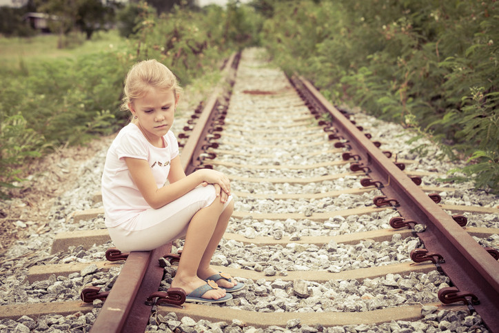 Sad young girl sitting alone on railroad tracks