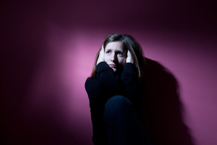 sad depressed woman crouching in dark room holding her head