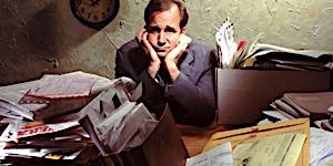 Businessman at desk piled with work and looking overloaded