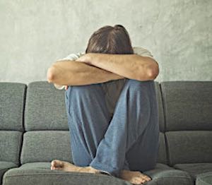 depressed man with head tucked into folded arms and legs