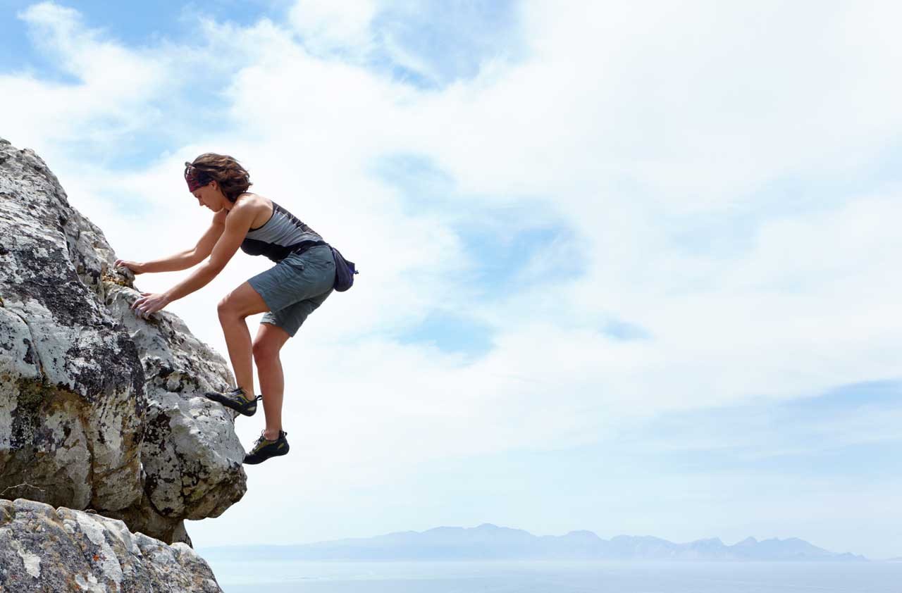 woman taking risks by climbing the side of a steep cliff