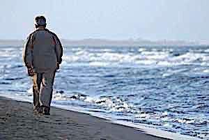 lonely sad older man walking alone by the shore