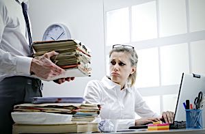 Man overloaded with work sits next to pile of papers