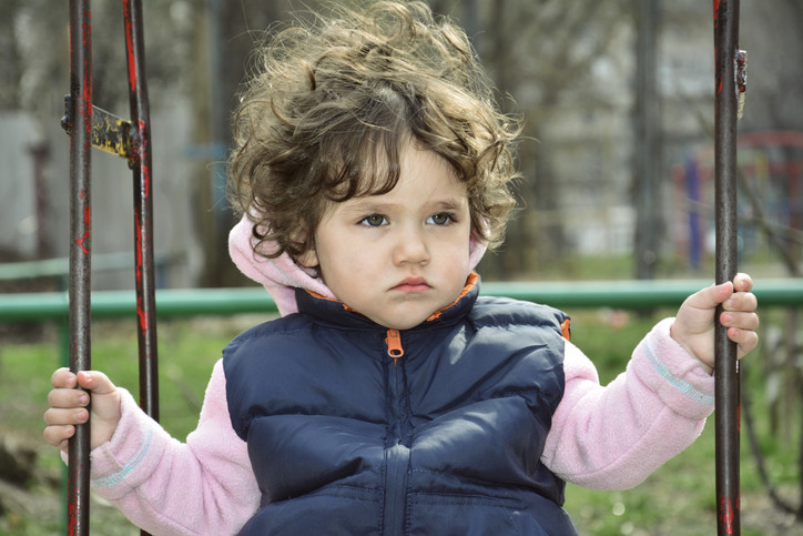 boy sitting on stopped swing showing no emotions