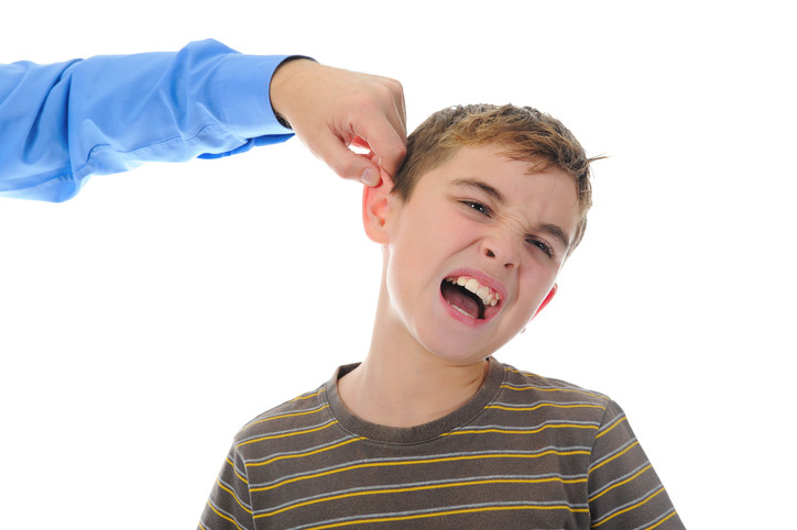 man pinching ear of boy who grimaces in pain
