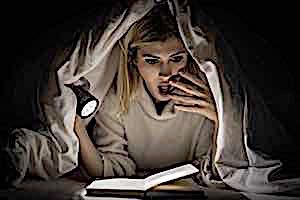 woman under covers expresses shock while reading book