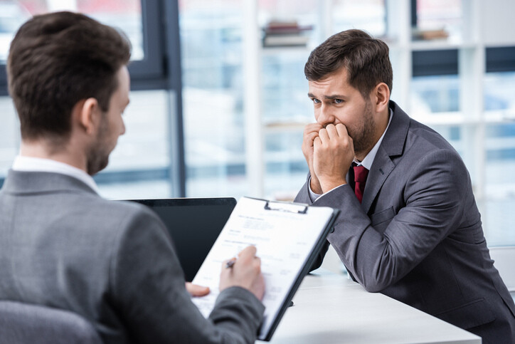 Nervous man in formal wear looking at businessman writing on clipboard during job interview