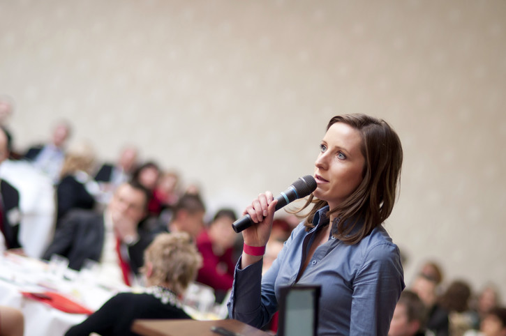 woman holds microphone while speaking to a group