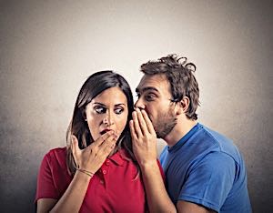 man whispering a secret into ear of shocked woman