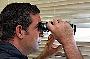 man with binoculars spying through window blinds