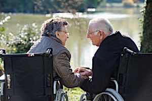 senior couple in wheelchairs longingly holding hands