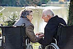 senior couple in wheelchairs longingly holding hands