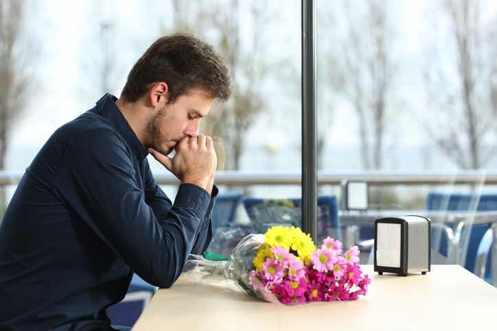 sad man with flowers alone at dinner table