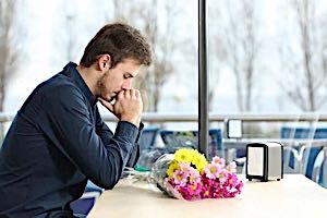 sad man with flowers alone at dinner table