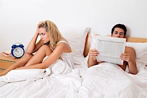 frustrated woman in bed with man reading paper