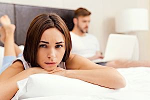 resentful woman in bed with man who is using computer