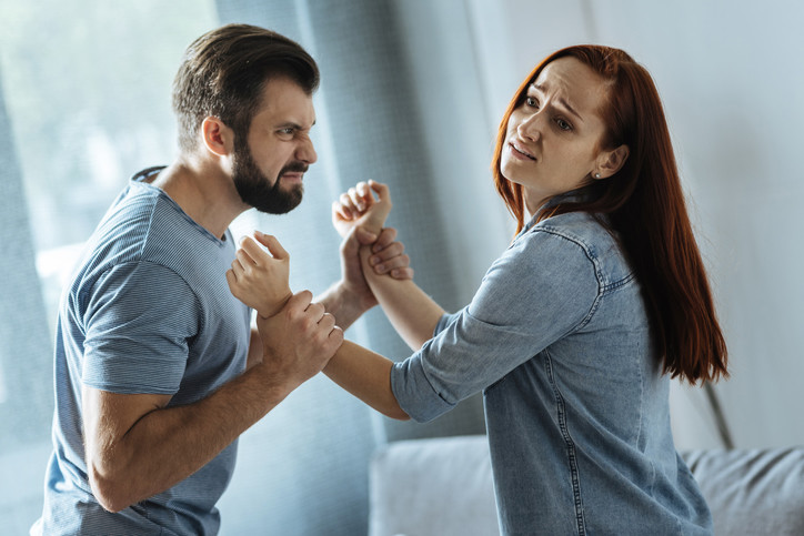 angry man grasps hands of fearful woman