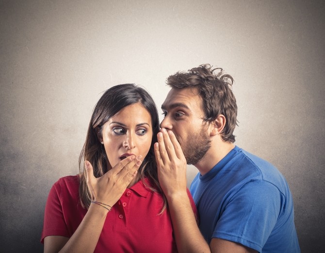 man whispering into astonished woman's ear
