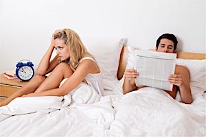 Upset  woman in bed with impotent man reading newspaper 