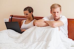sexually frustrated man in bed with woman on computer who ignores him